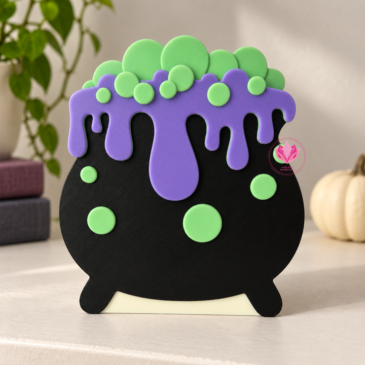 Black 3D printed cauldron drip box with purple drips and bright green bubble accents, displayed on a tabletop.