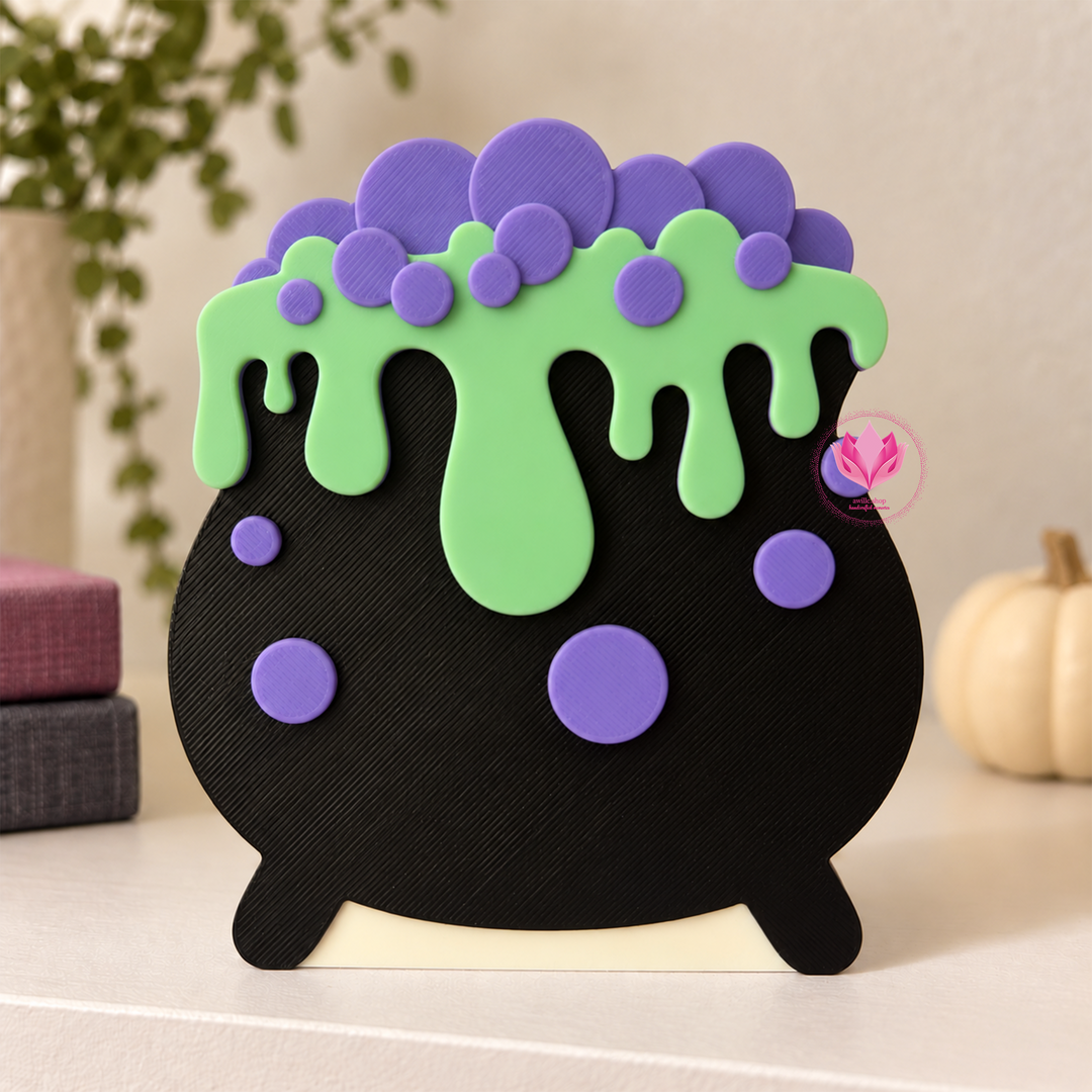 Black 3D printed cauldron drip box with bright green drips and purple bubble accents, displayed on a tabletop.