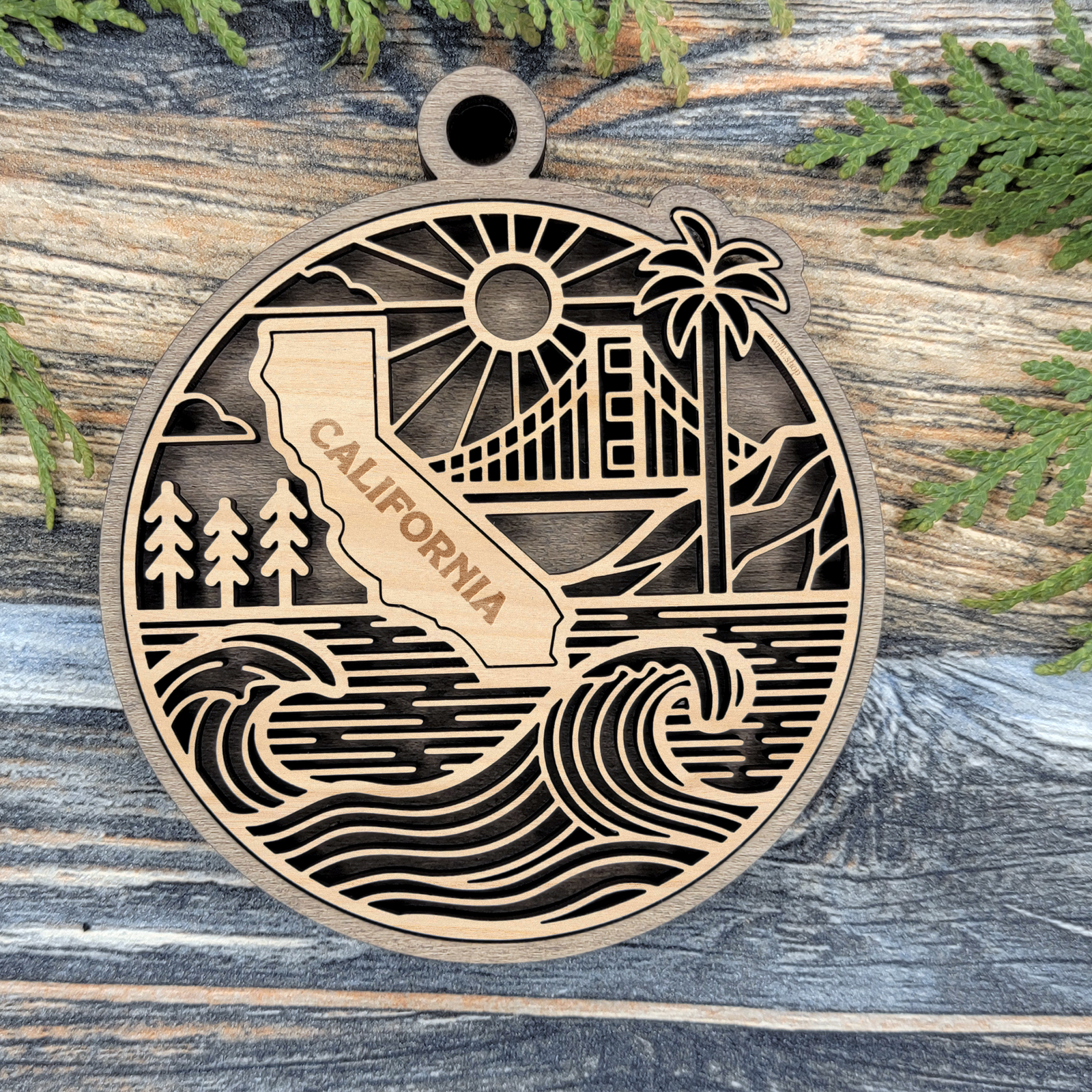 Layered California wood ornament with a laser cut Golden Gate Bridge, palm tree, redwoods and ocean waves around the state shape