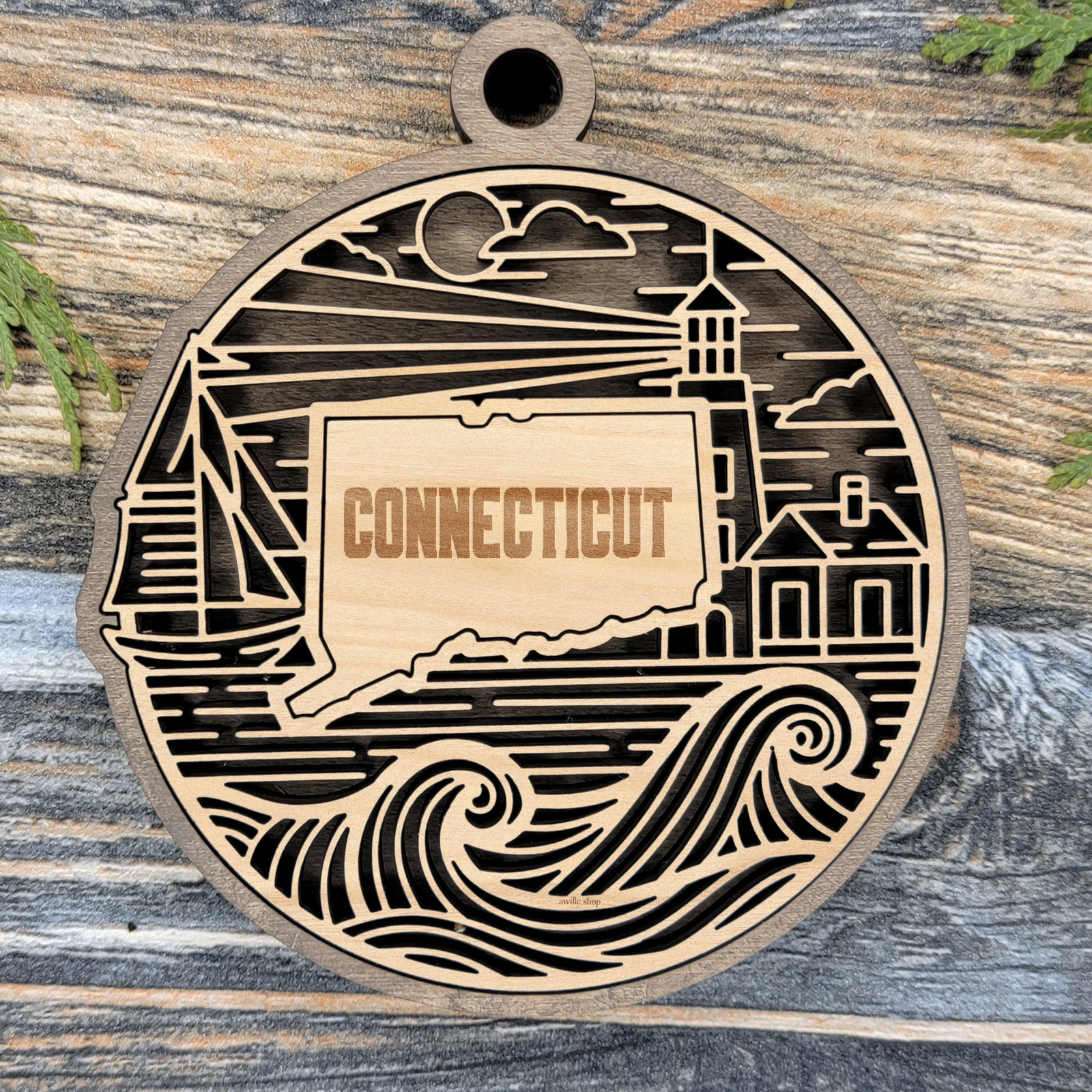 Layered Connecticut wood ornament with a laser cut lighthouse, sailboat, coastal cottage and ocean waves framing the engraved state shape