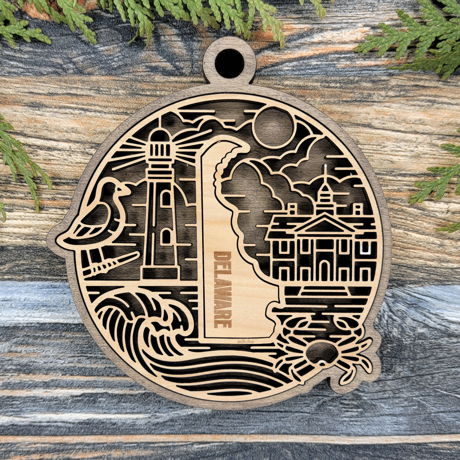 Layered Delaware wood ornament with a laser cut lighthouse, seagull, capitol building, crab and ocean waves framing the engraved state shape