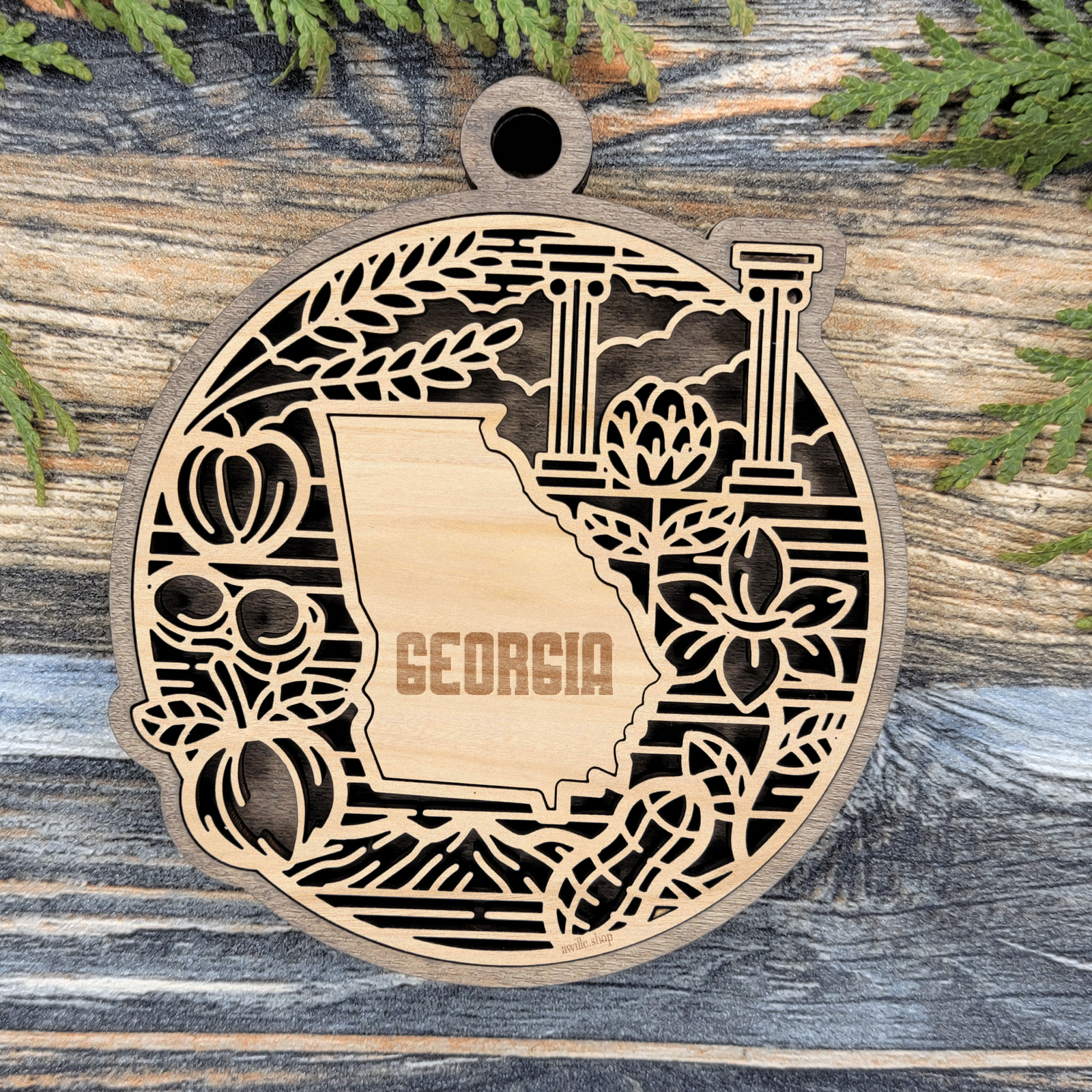 Layered Georgia wood ornament with a laser cut wheat, columns, peaches and a magnolia blossom framing the engraved state shape