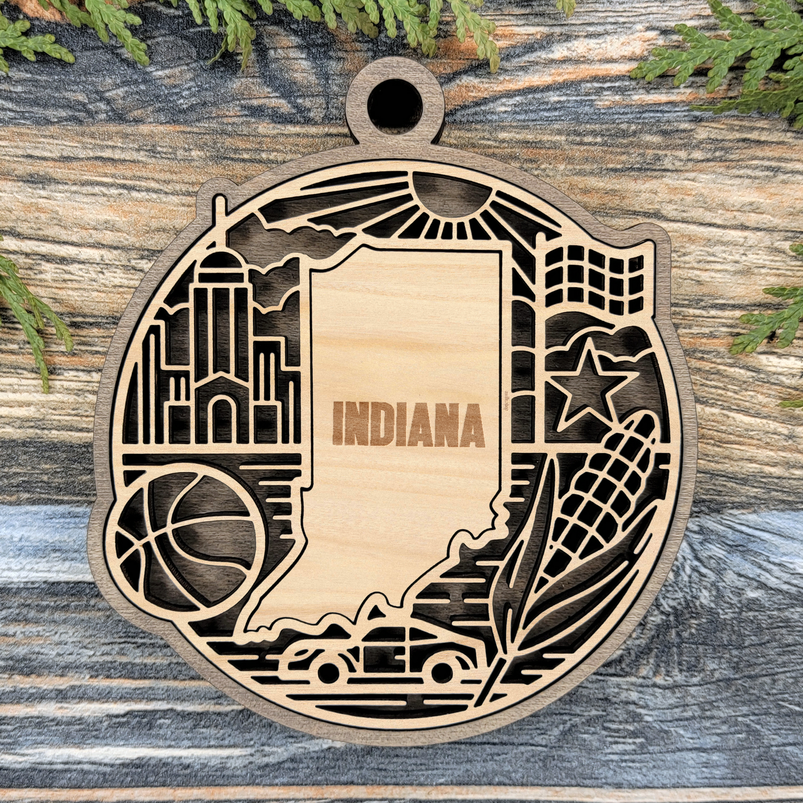 Layered Indiana wood ornament with a laser cut basketball, checkered racing flag, race car, corn and a star framing the engraved state shape