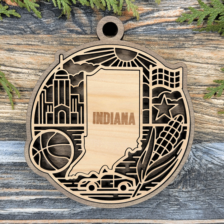 Layered Indiana wood ornament with a laser cut basketball, checkered racing flag, race car, corn and a star framing the engraved state shape