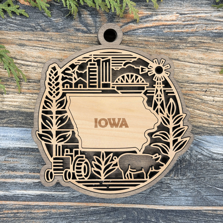 Layered Iowa wood ornament with a laser cut wheat, a windmill, a tractor and a pig framing the engraved state shape