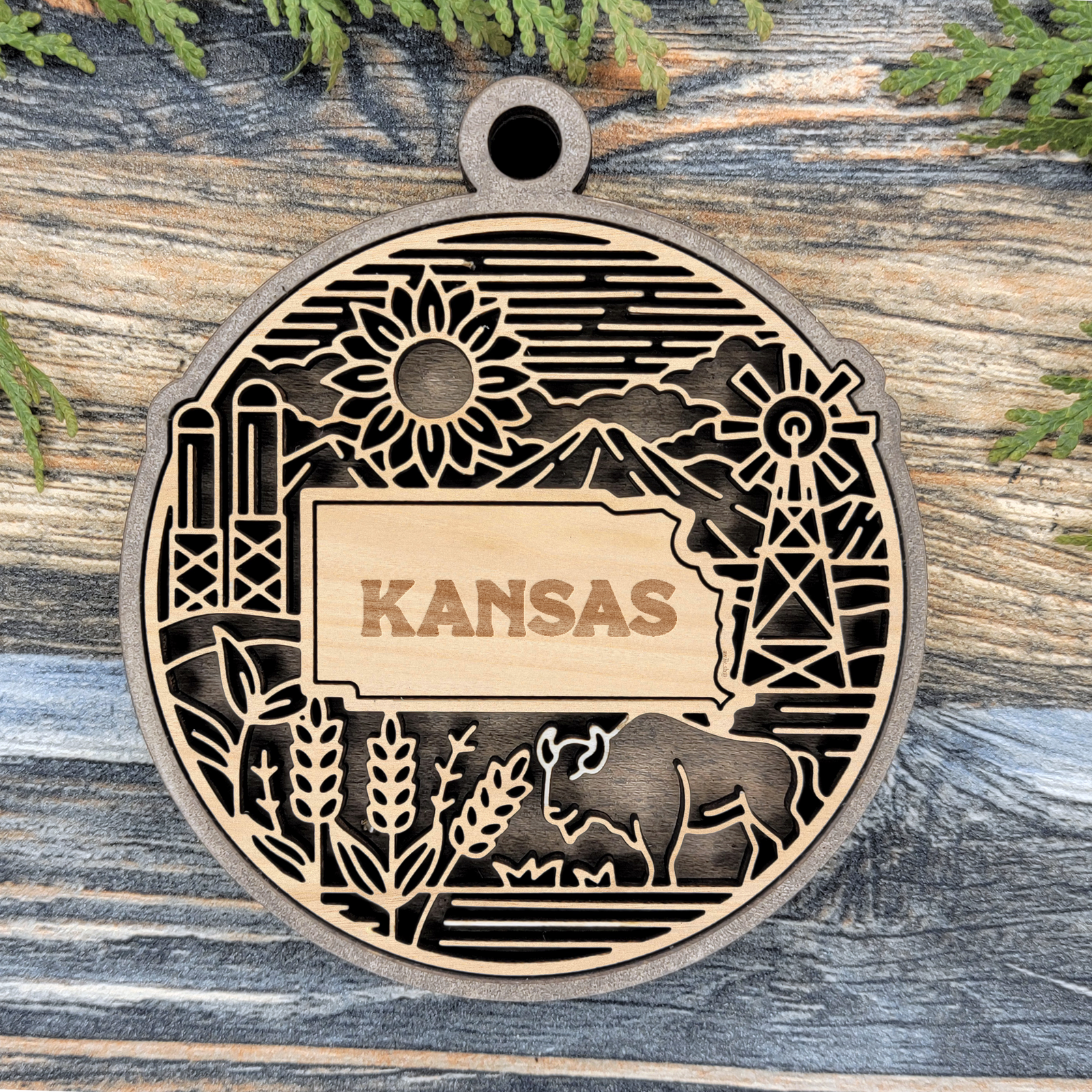 Layered Kansas wood ornament with a laser cut sunflower, grain silos, a windmill, wheat and a bison framing the engraved state shape