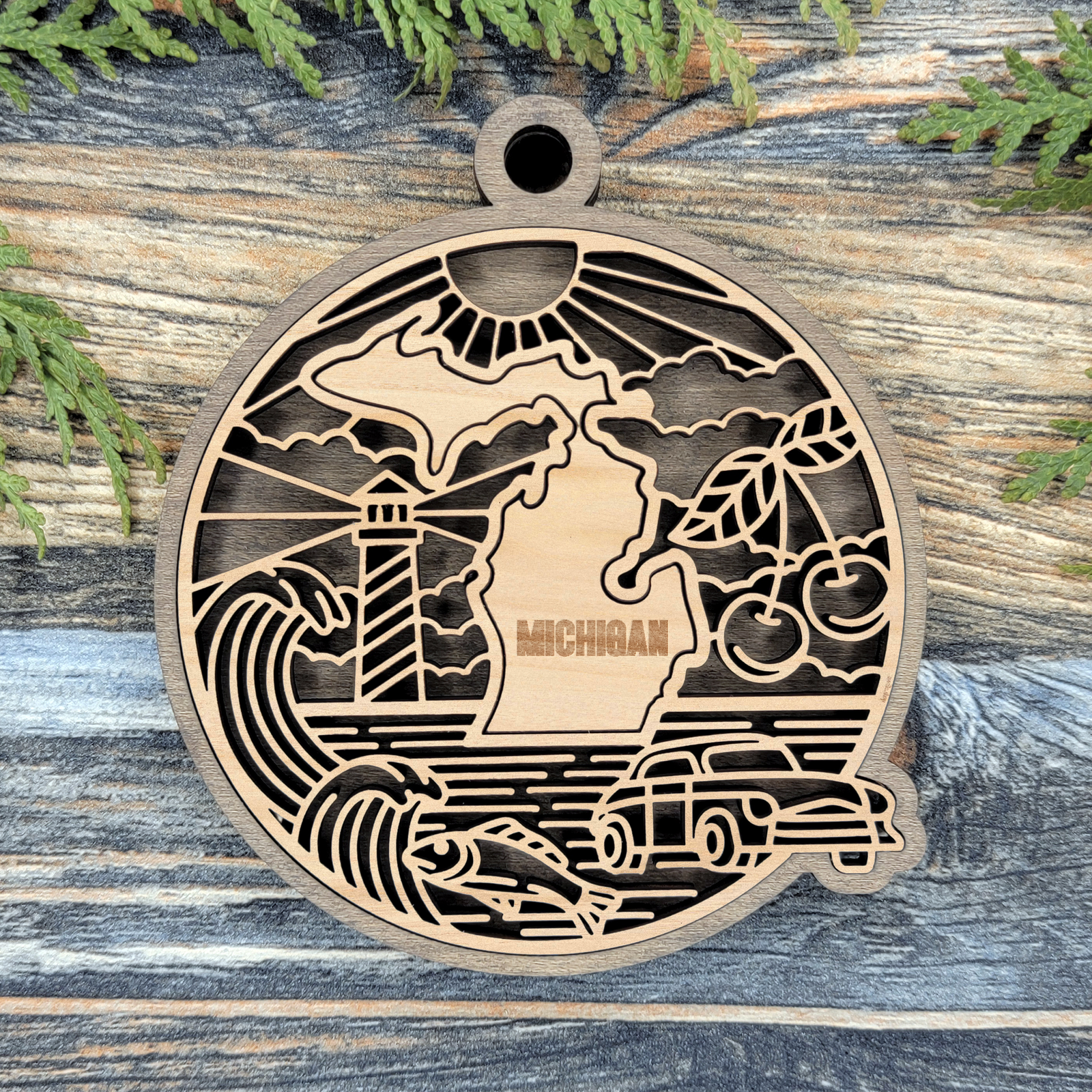 Layered Michigan wood ornament with a laser cut lighthouse, cherries, a classic car and a fish framing the engraved state shape
