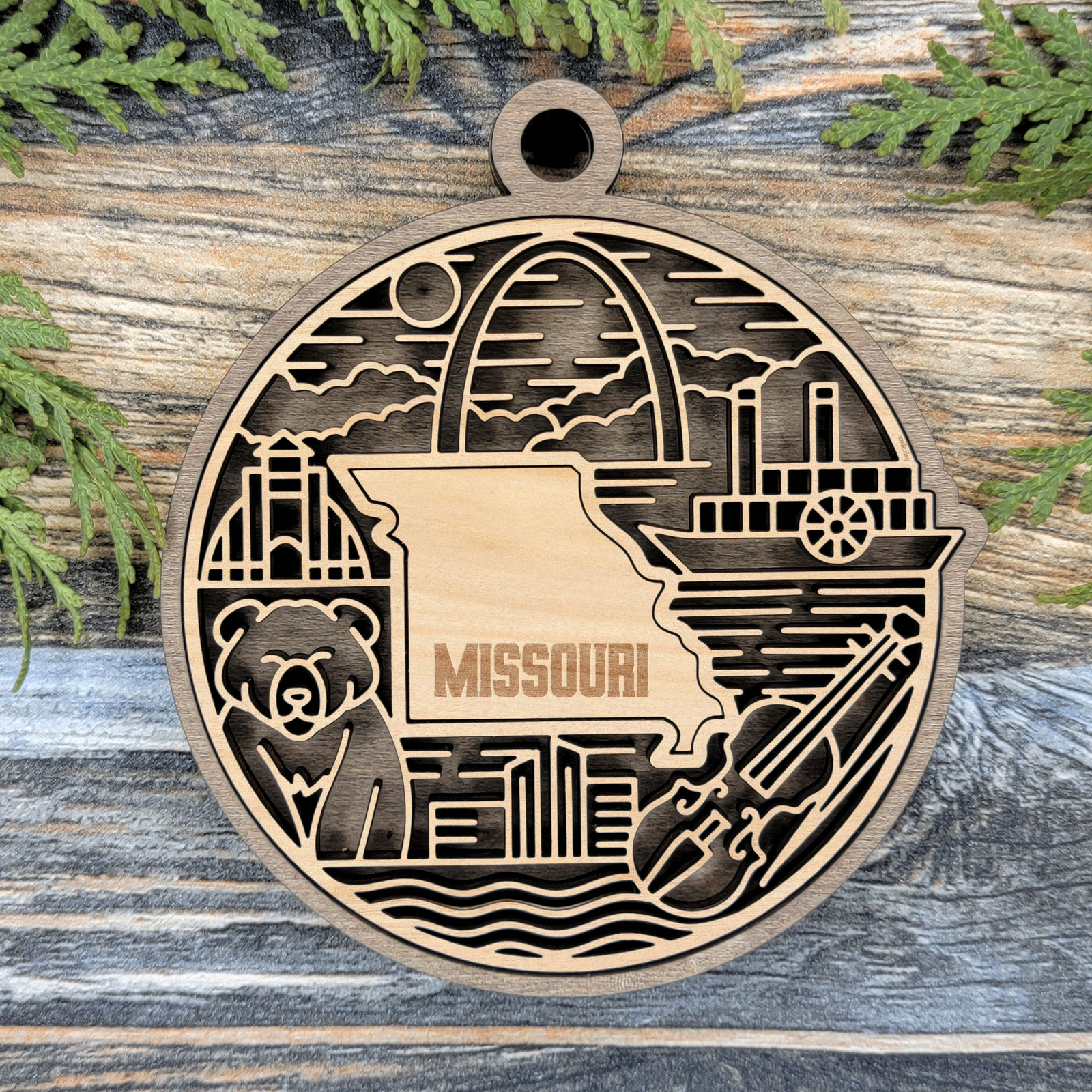 Layered Missouri wood ornament with a laser cut Gateway Arch, a riverboat, a bear and a fiddle framing the engraved state shape