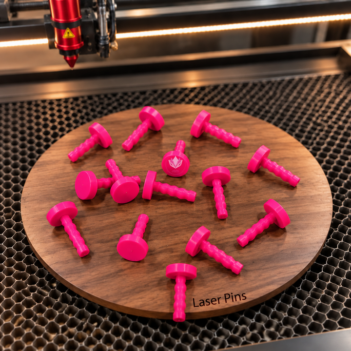 Bright pink 3D printed laser honeycomb bed pins arranged on a round wooden board marked Laser Pins inside a laser cutter.