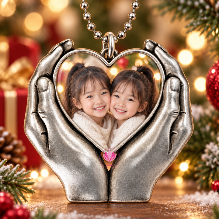 Close-up of a personalized heart-hand photo charm featuring two smiling children, hanging among Christmas greenery and lights.